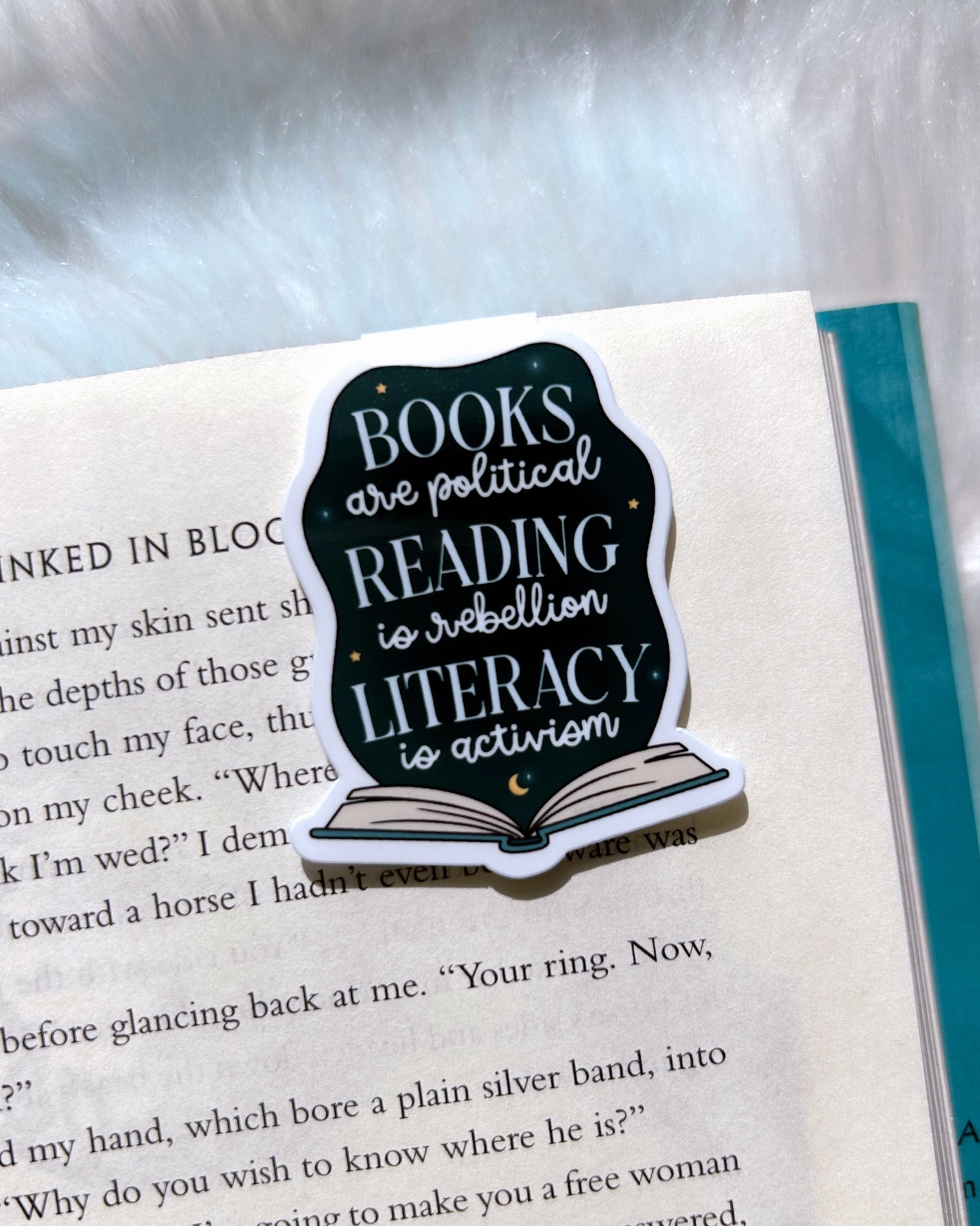 A magnetic bookmark placed on an open book. The bookmark has text related to the theme of books and politics.