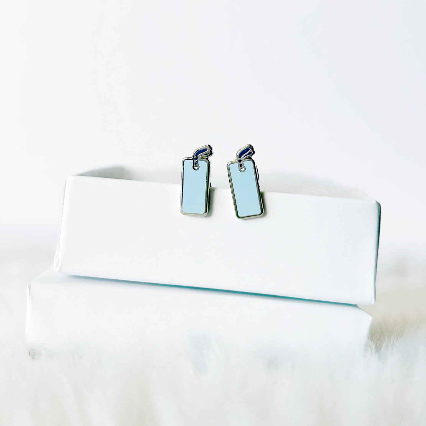 Pair of light blue earrings on a white cushion with a white background