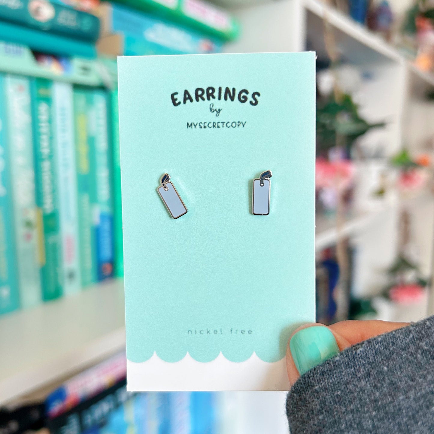 Earring packaging with 'Earrings by My Secret Copy' on a blurred store shelf background