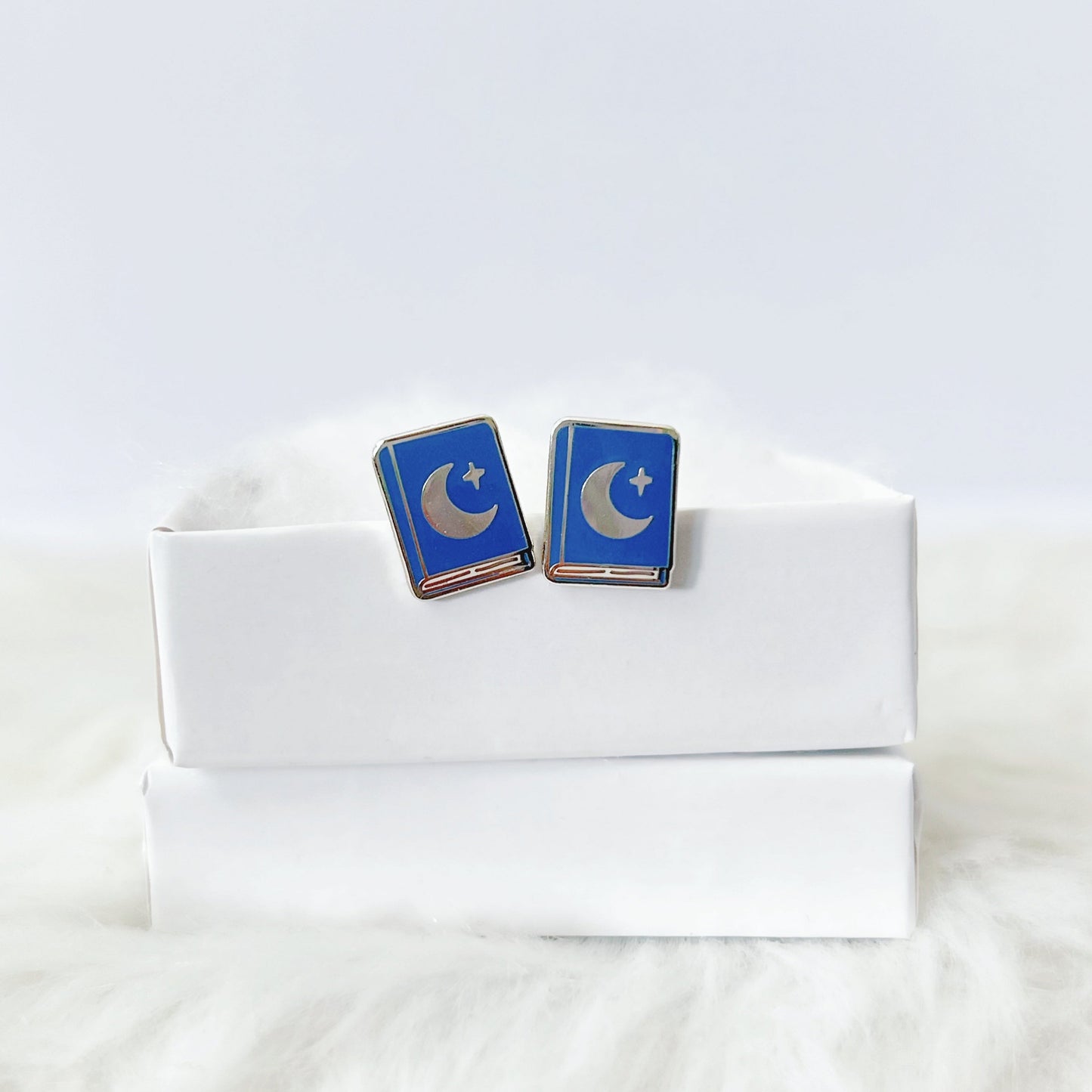 Blue and silver earrings on a white box with a white fur background