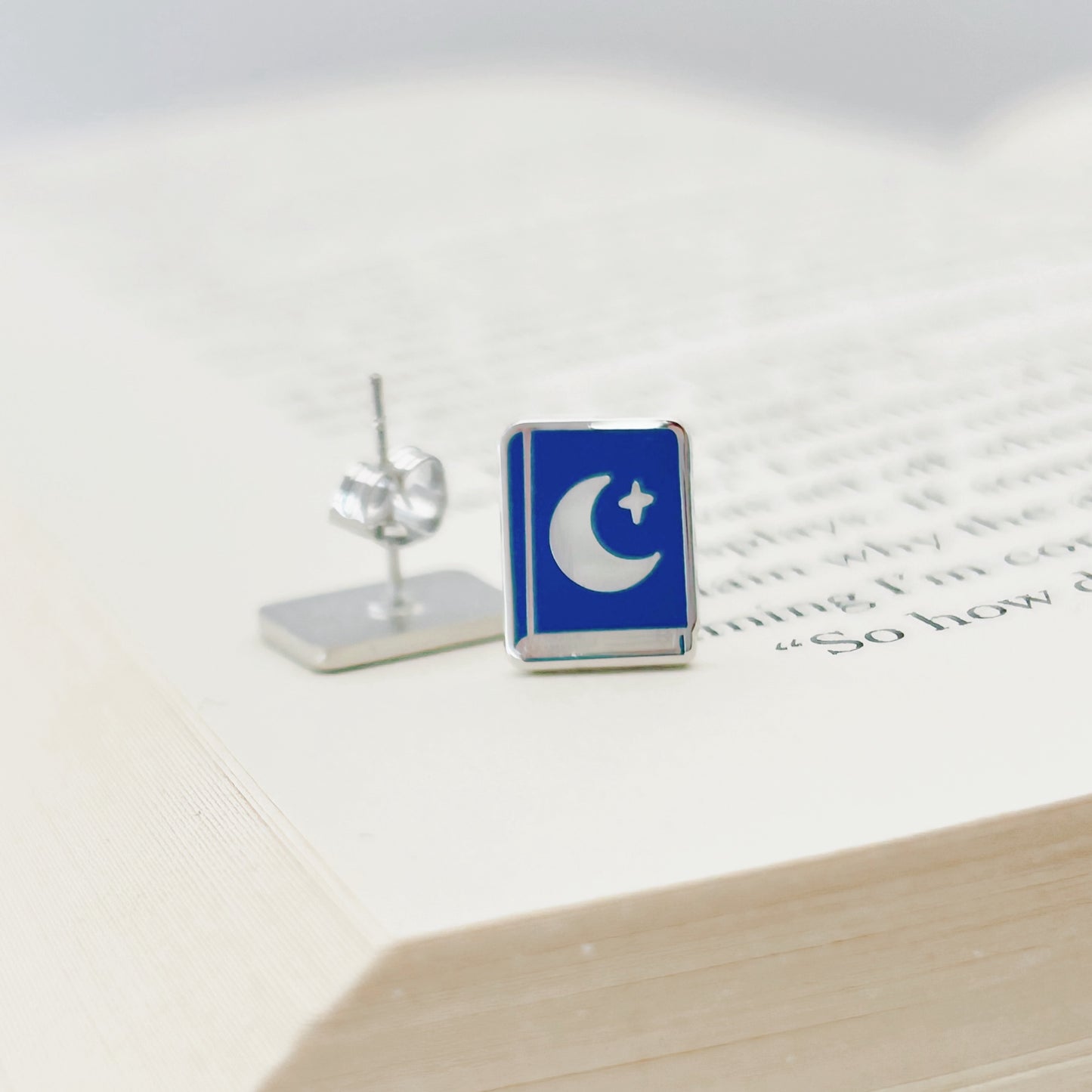Blue and silver rectangular earring on a white surface with text