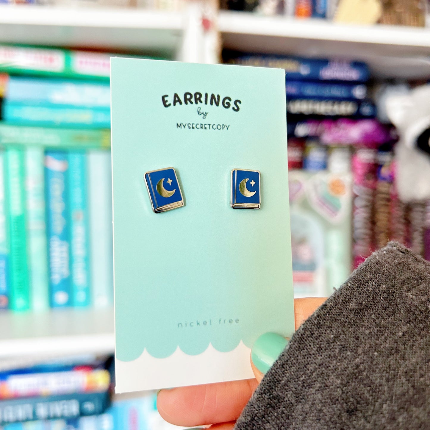 Earring card with moon and star earrings held in front of a bookshelf.