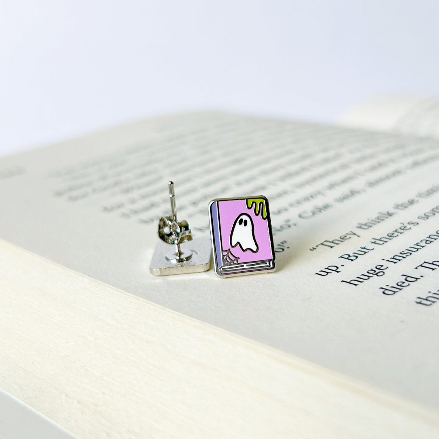 Two small ghost earrings on an open book with a white background
