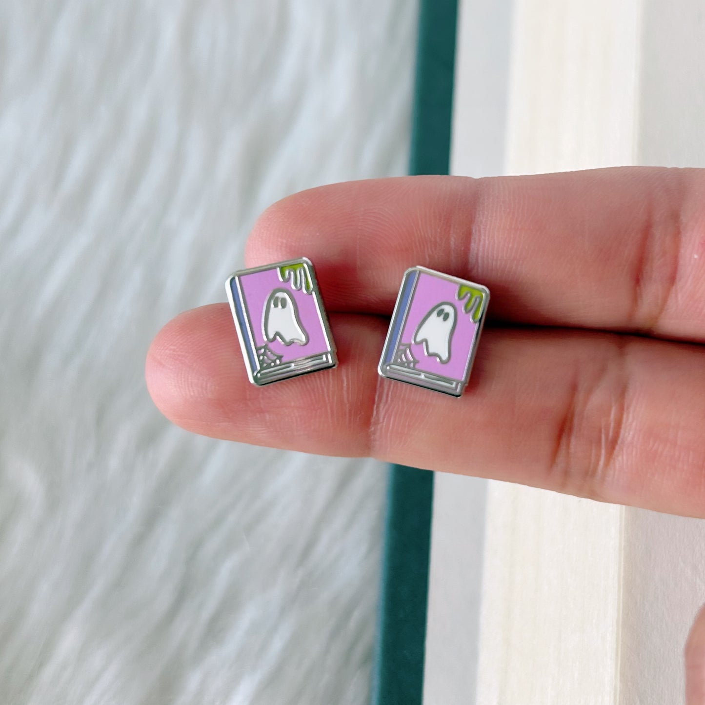 Pair of ghost-themed earrings held between fingers against a neutral background