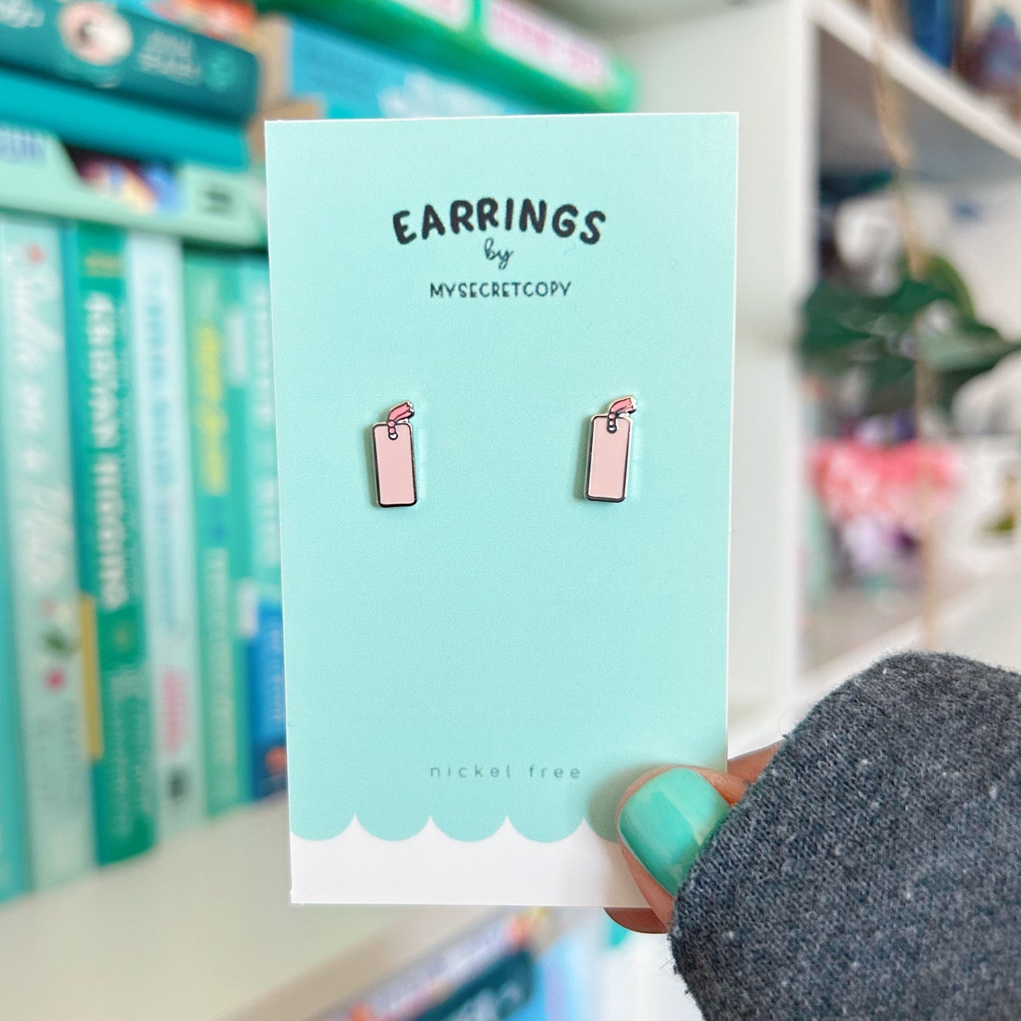 Card with earrings design held by a hand in front of a bookshelf