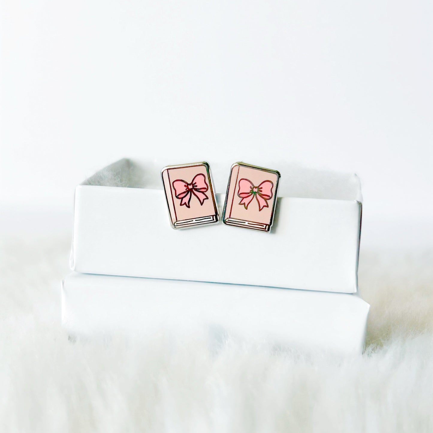 Book-shaped earrings with pink ribbons on a white surface