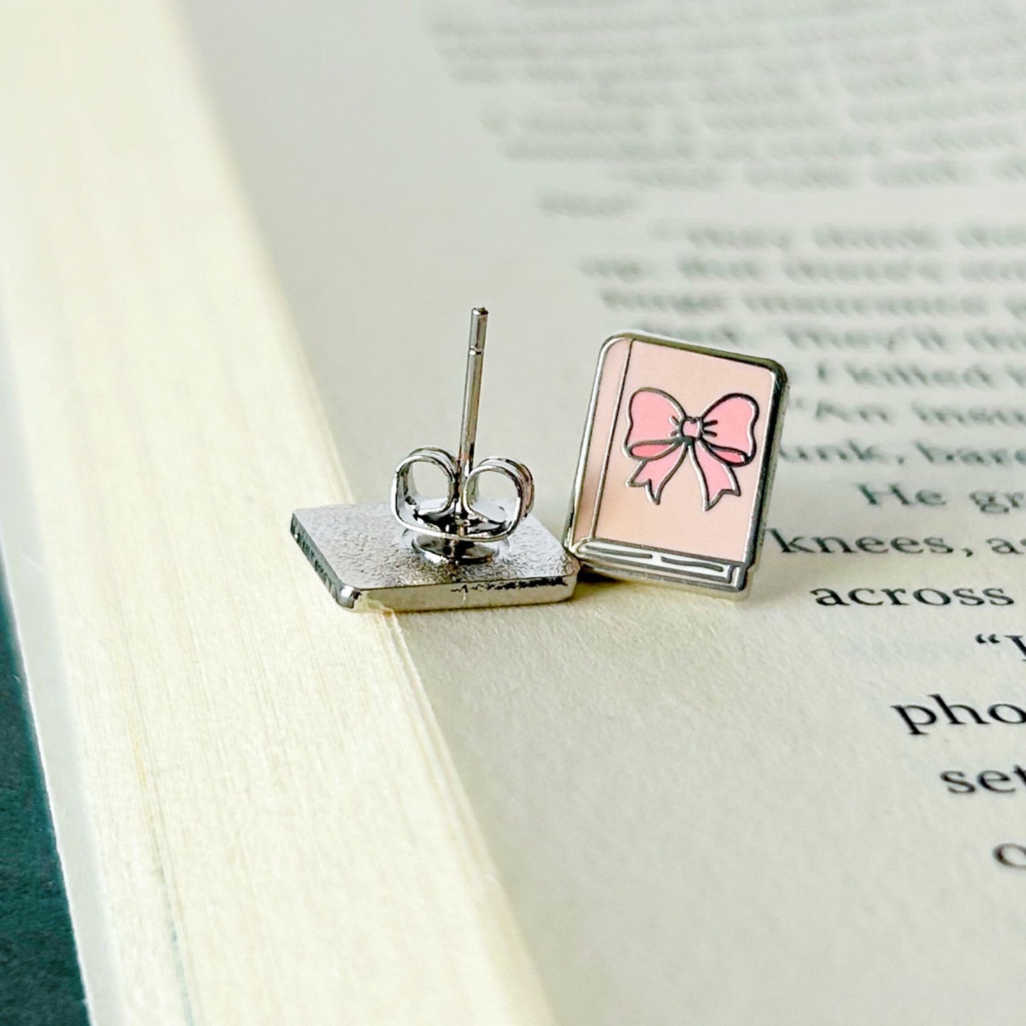 Pair of earrings with a pink bow design on an open book