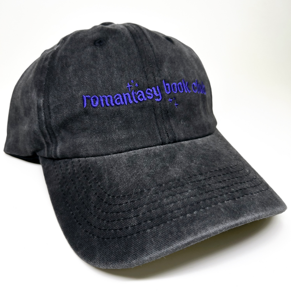 A baseball cap with purple embroidered text reading 'romantasy book club' on the front, shown against a plain white background.