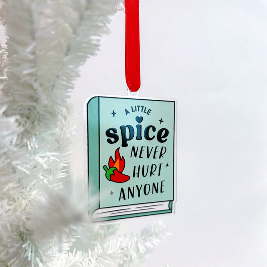 Decorative ornament with a book design and text 'A little spice never hurt anyone' on a white Christmas tree.