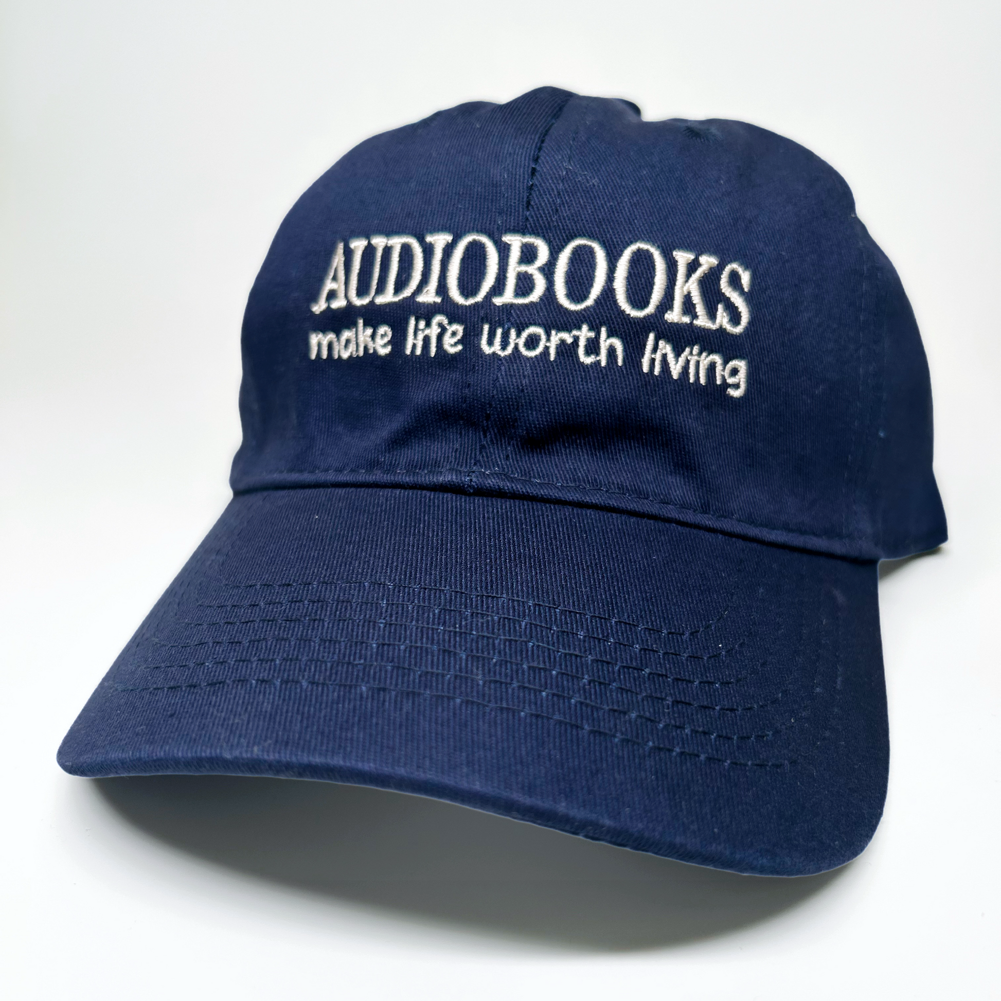 A navy blue baseball cap with white embroidered text reading 'AUDIOBOOKS make life worth living' on the front, photographed on a clean white background.