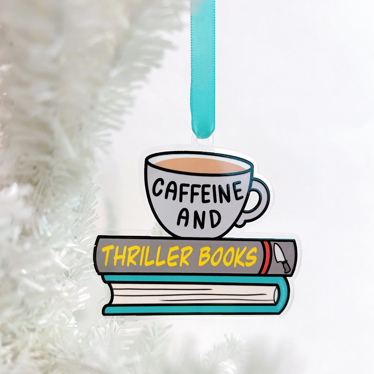 Decorative ornament with a cup labeled 'Caffeine' and books labeled 'Thriller Books' on a white fluffy background.