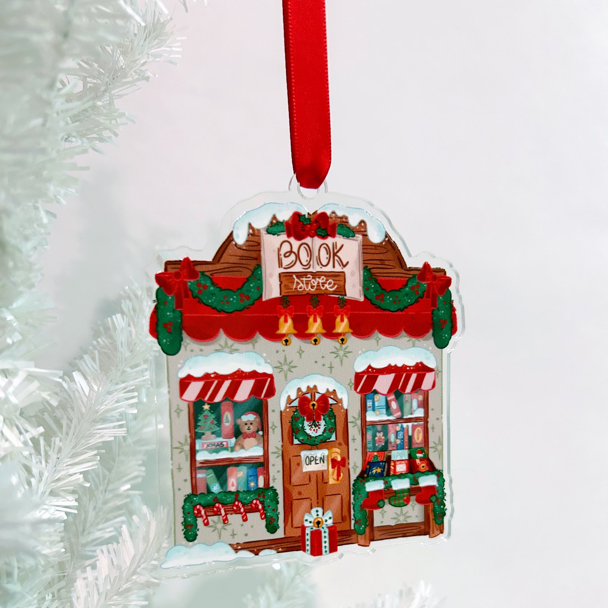Decorative Christmas ornament shaped like a bookstore with a red ribbon on a white background.