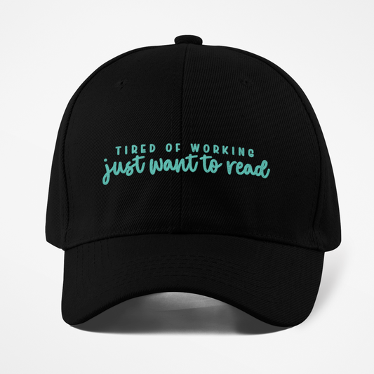 Black cap with teal text 'Tired of working just want to read' on a white background