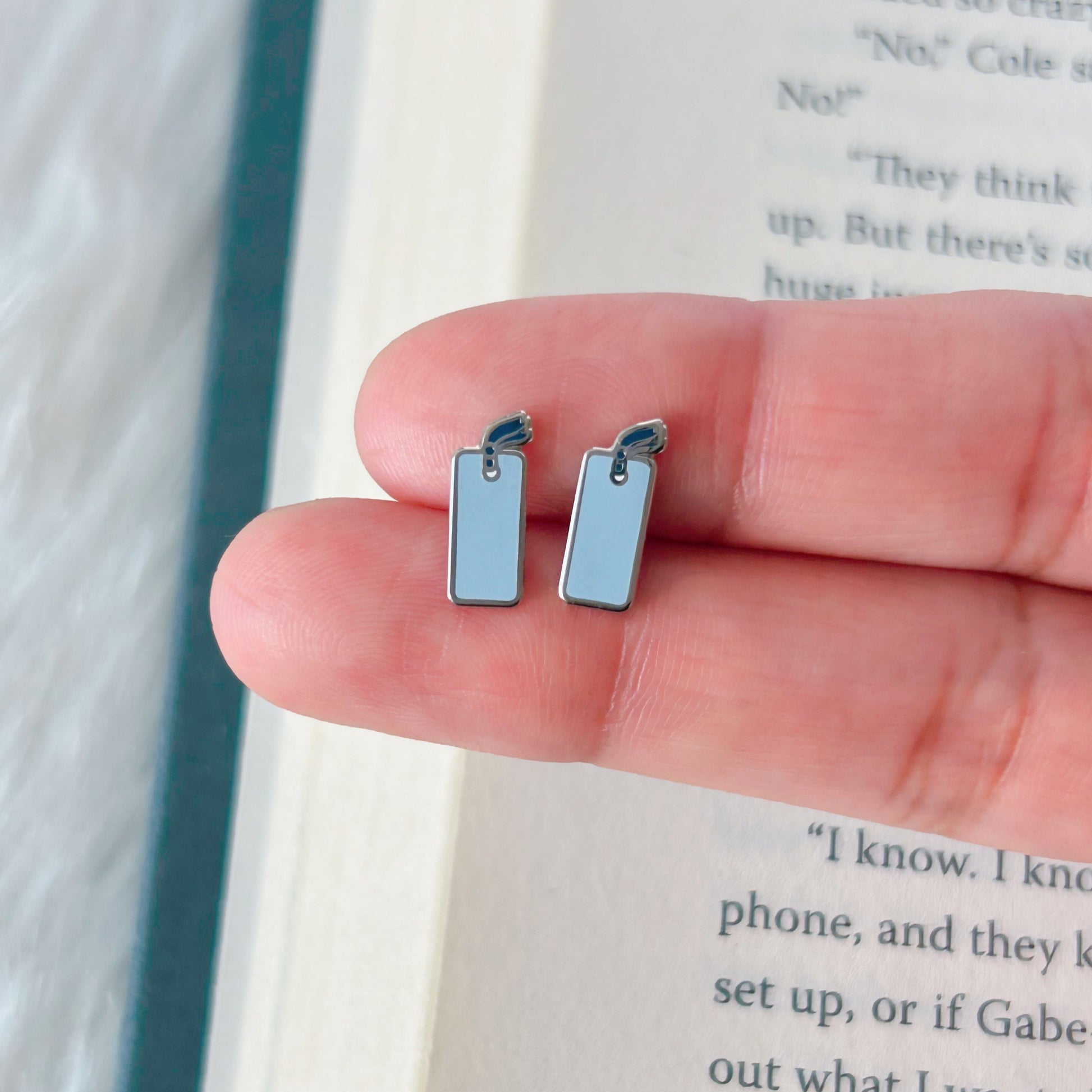 blue rectangular earrings held between fingers against a book background