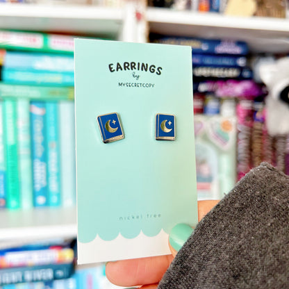 Earring card with moon and star earrings held in front of a bookshelf.