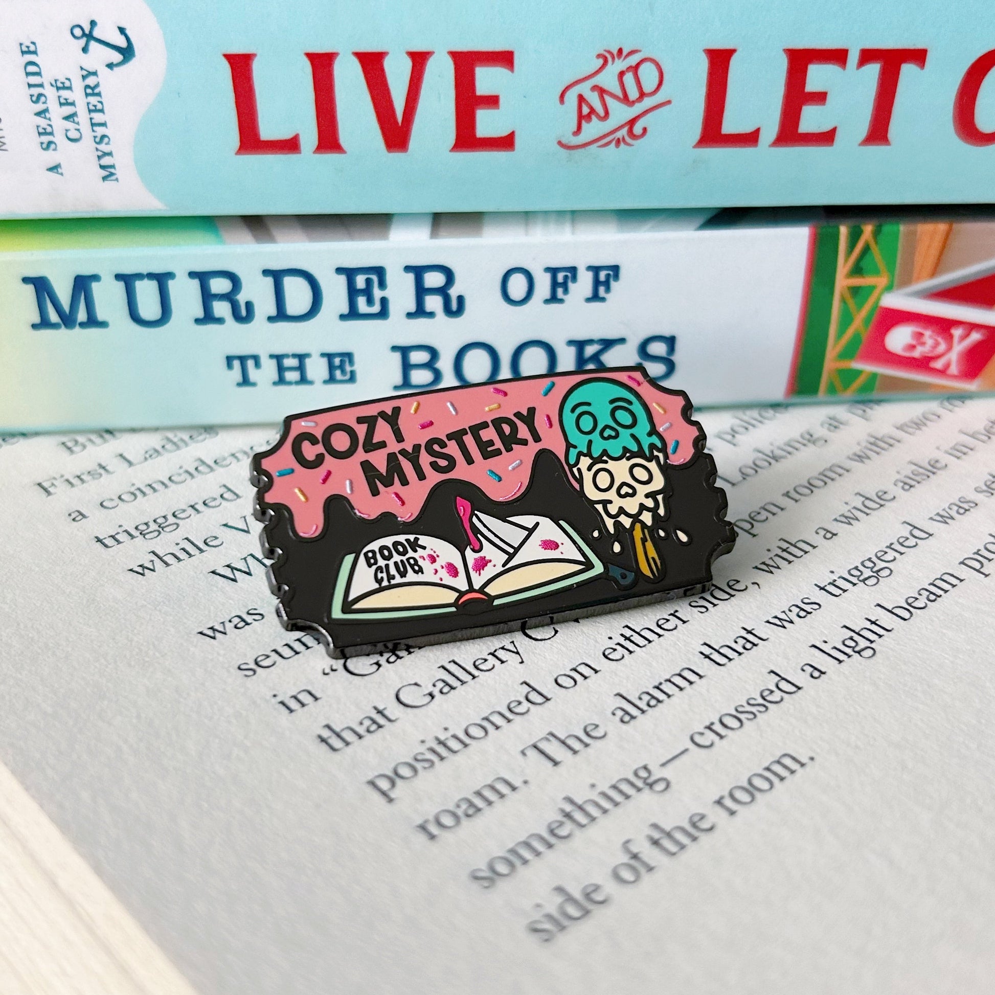 Pin with 'Cozy Mystery' design on a stack of books titled 'Live and Let Die'.