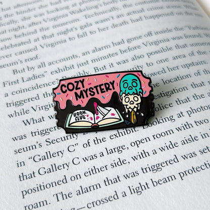 cozy mystery enamel pin on an open book