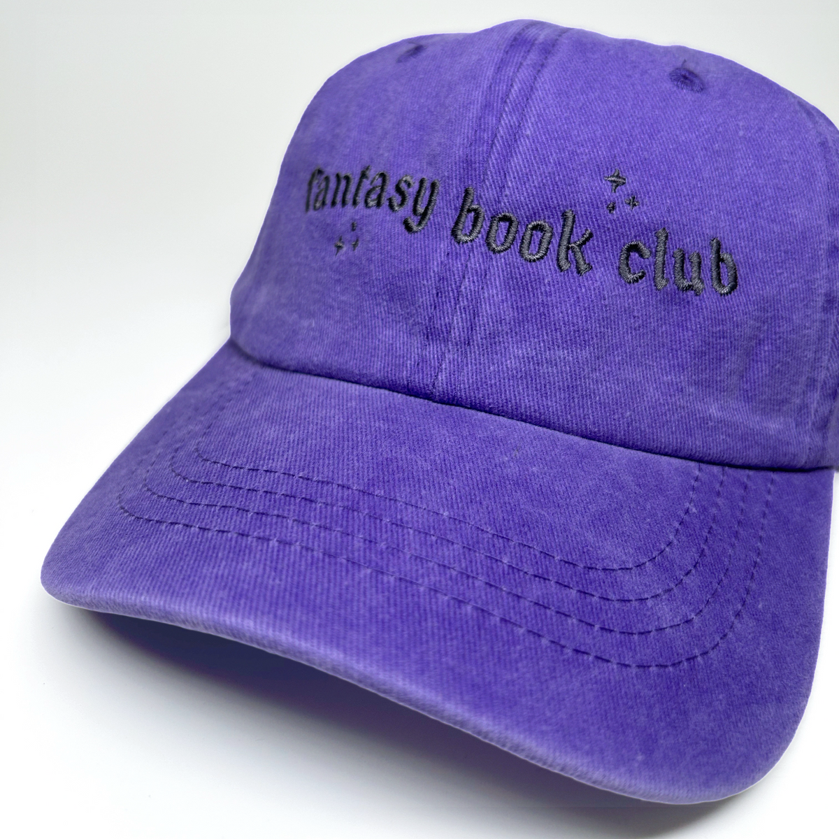 A purple cotton baseball cap with 'fantasy book club' embroidered in black across the front, shown on a clean white background.