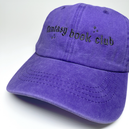 A purple cotton baseball cap with 'fantasy book club' embroidered in black across the front, shown on a clean white background.