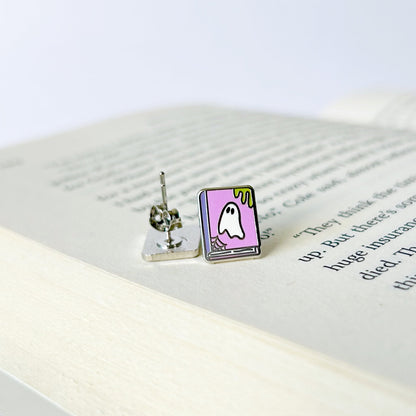 Two small ghost earrings on an open book with a white background
