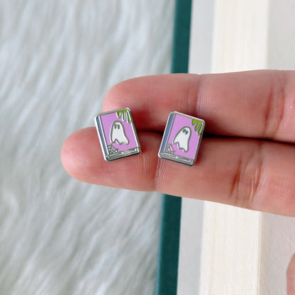 Pair of ghost-themed earrings held between fingers against a neutral background