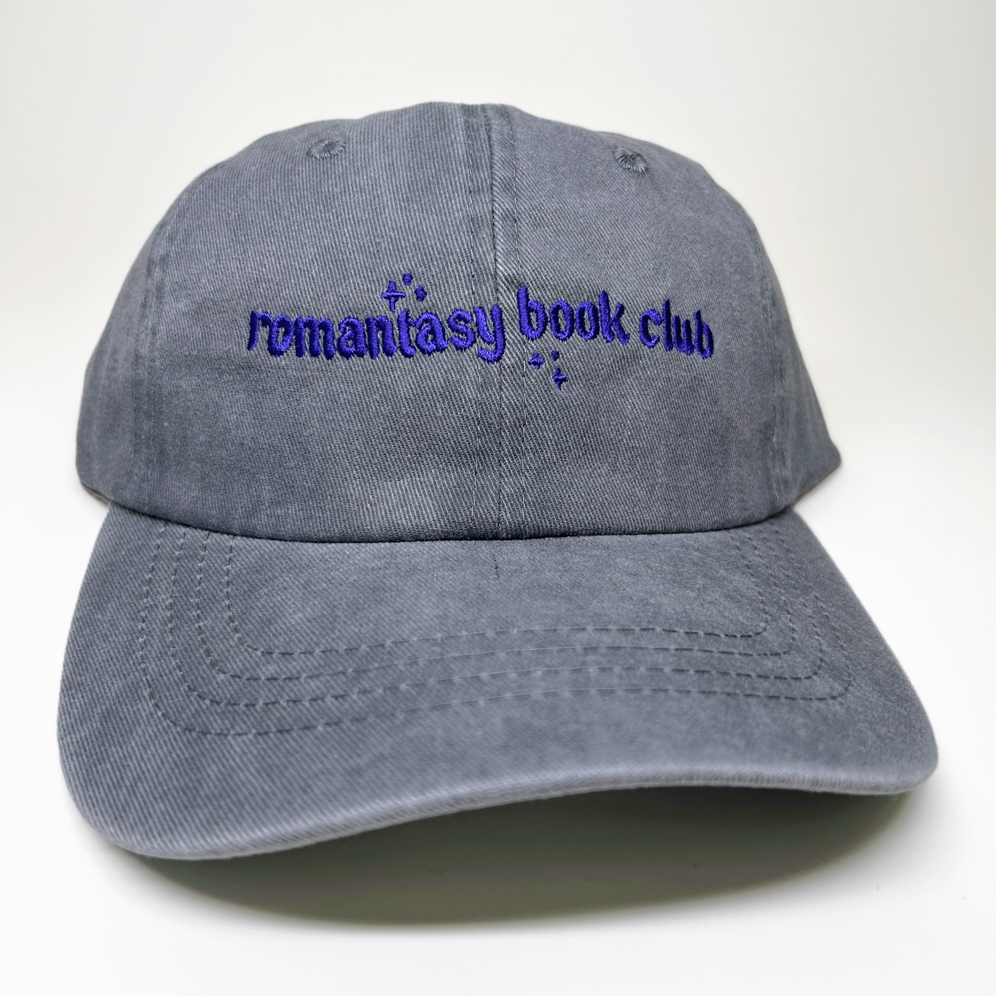 A gray washed cotton baseball cap with 'remantasy book club' embroidered in purple on the front, shown against a plain white background.