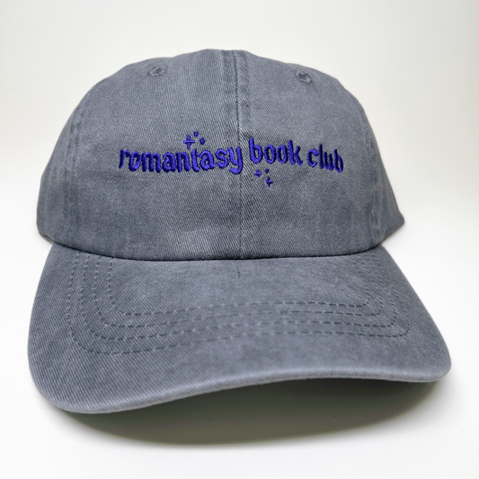 A gray washed cotton baseball cap with 'remantasy book club' embroidered in purple on the front, shown against a plain white background.