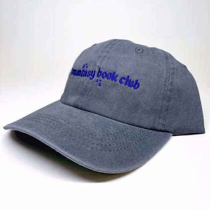 A washed slate blue baseball cap with 'romantasy book club' embroidered in blue cursive text on the front, shown on a white background.