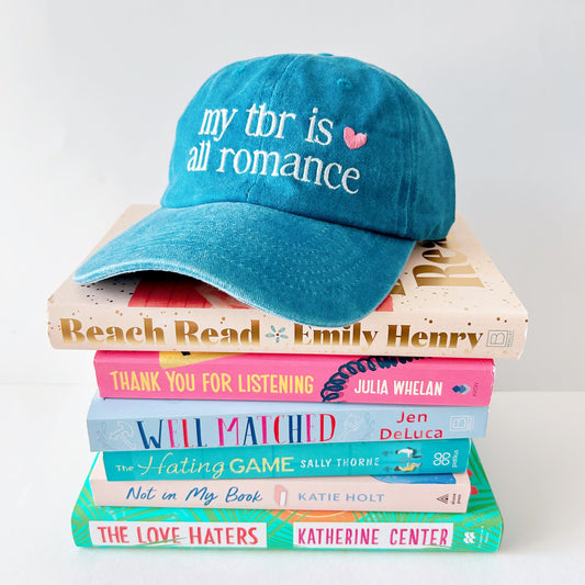 Blue cap with 'my tbr is all romance' text on a stack of books