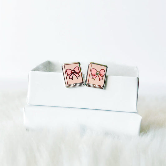 Book-shaped earrings with pink ribbons on a white surface