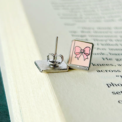 Pair of earrings with a pink bow design on an open book