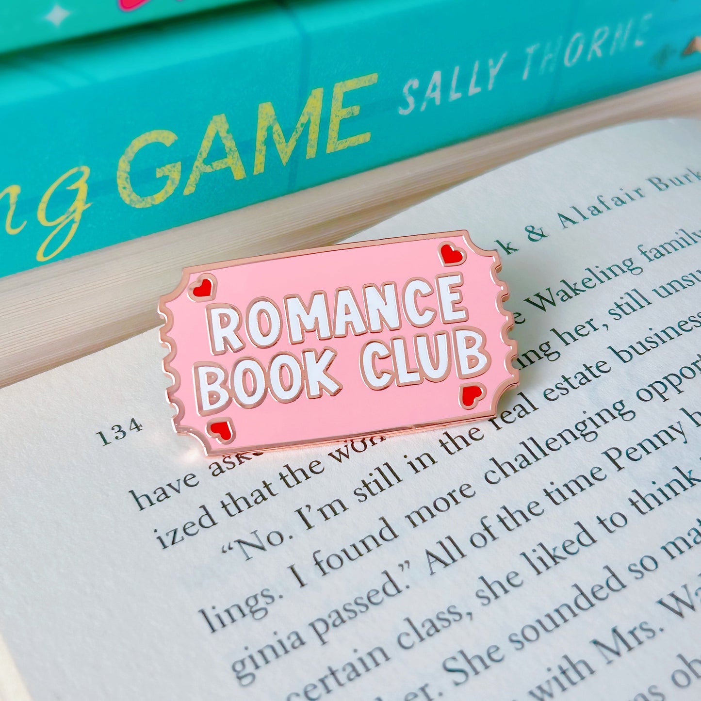 Pink enamel pin with 'Romance Book Club' text on an open book