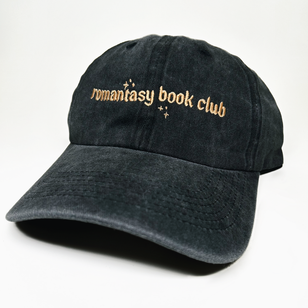 A black washed cotton baseball cap with 'romantasy book club' embroidered in gold across the front, set against a plain white background.